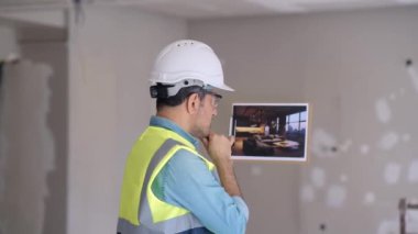 Profesyonel mühendis, modern oturma odası tasarımlı, koruyucu kasklı ve batılı bir adamla resme bakıyor. Yenileme işleminden sonra evin içini hayal ediyor.