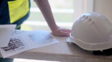 Odaklanmış profesyonel üniforma uzmanı apartmandaki oda yenileme işlemi sırasında inşaat güvenlik ekipmanlarının yanında duran belgelerle çalışıyor.