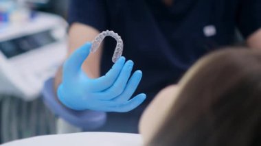 Uzman ortodontist, ısırık düzeltme için tasarlanmış yenilikçi dizilimleri kauçuk eldivenli kamera doktoruna gösteriyor ki dişler için modern şeffaf kapaklar