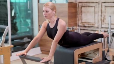 Spor salonunda profesyonel pilates eğitimi. Kollarını ve omuzlarını geren sarışın kadın. Reformcu kadın üzerinde etkili egzersiz yapıyor.