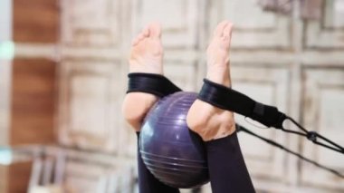 Pilates eğitimi gören kadın spor aletleriyle profesyonel antrenman yapan pilates yaparken spor topunu kullanıyor.