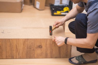 Mobilya montajı yapan marangoz akıllı saatle ev içi üniforma ustası için ahşaptan yapılmış küçük bir dolaba çivi çakıyor.