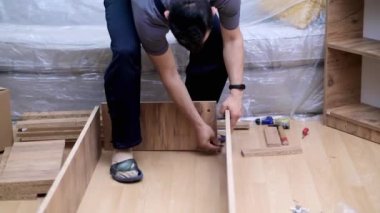 Marangozluk işi ve işçi işçi tulumları içinde, mobilya montaj sürecini müşteri dairesine yerleştirmek için ahşap dolaba çivi çakıyor.