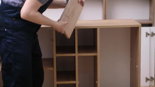 家具の出荷と近代的なオフィスのプロの木工結果の男の家具の組み立てを終えたラックに木製の棚を置く大工を固定 — ストック動画