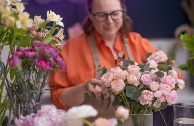 Yetenekli bayan çiçekçi ve işyeri sahibi güzel bir buket renkli çiçek hazırlıyor ve iç çiçekçisine renk ve güzellik katıyor..