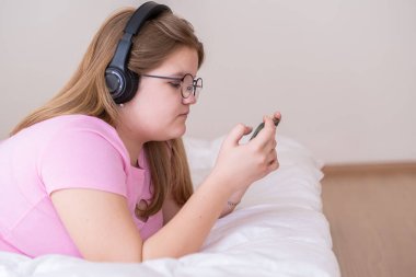 Rahat genç kız akıllı telefondan mesajları kontrol ediyor. Kulaklıkla müzik dinliyor. Aşırı kilolu genç kız yatakta uzanmış sosyal ağlardan ve evde en sevdiği şarkıdan hoşlanıyor.
