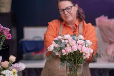 Çiçekçi dükkanında önlük takan yetenekli bir kadın çiçekçi muhteşem bir çiçek buketi yapmaya hazırlanıyor.