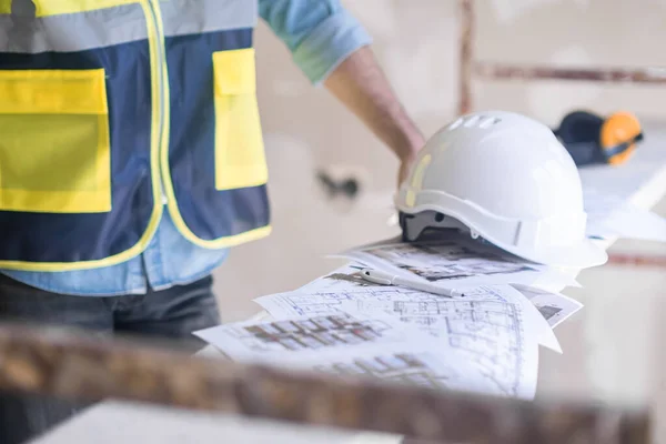 stock image Worker in professional uniform putting hardhat on heap of project documents construction equipment and safety rules during renovation process in premise