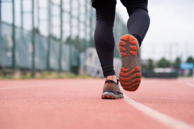 Spor ayakkabılı bir sporcu, açık hava stadyumunda kapalı alanda spor yaparken kentsel alanda marifetli bir koşucuda kırmızı lastik pist boyunca koşuyor.