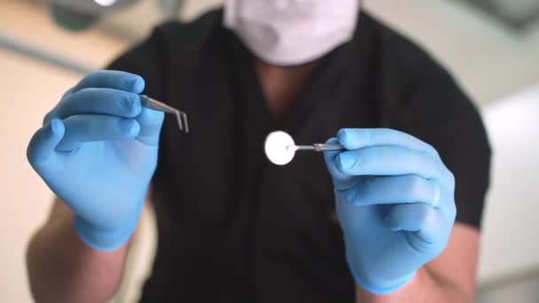 口腔科中心牙齿护理过程中 穿着黑色制服的熟练男牙医用金属钳和圆形镜片检查病人口腔 — 图库视频影像