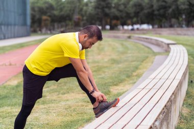 Sarı tişört giyen, spor ayakkabı bağlayan, spor sahasında bankta uzanan, bahar şehir parkında koşan, antrenmanda ayak takımlarını ayarlayan bir adam.