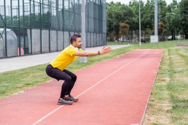 Rahat giysiler içindeki sporcu elleri koşu parkındaki halk stadyumunda koşuya uzanan çömelme hareketleri yapıyor.