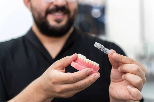 Gülümseyen doktor, diş sağlığı kliniğinde diş düzeltme metodunu sunan plastik insan çene modeline düzgün hizalayıcılar yerleştiriyor.