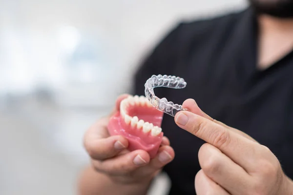 Doktor, stomatoloji kliniğinde diş geliştirme konusunda basit ve etkili bir cihaz göstermek için plastik alt çene modeline temiz hizalayıcılar yerleştiriyor