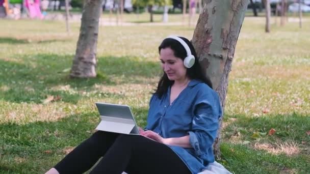 Wanita Muda Dengan Komputer Tablet Dan Earphone Nirkabel Duduk Halaman — Stok Video
