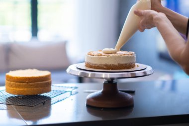 Kadın el yapımı kek yapıyor, üzerine taze beyaz krema koyuyor pasta külahında yetenekli ev hanımı mutfak masasında duruyor ve ev yapımı leziz pastaları hazırlıyor.