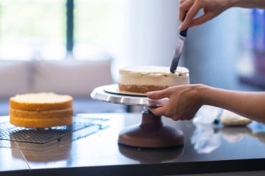 Doğum günü kutlaması için el yapımı şekerlemeler hazırlayan yetenekli bir pastacı. Mutfak katmanlarına organik beyaz krema sürmüş bir kadın.
