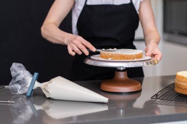 Siyah önlüklü kadın organik şekersiz kek tabaklarını lezzetli kremayla süpürüyor mutfak gereçleri kullanarak düğün kutlaması için özel hamur işi yapıyor.