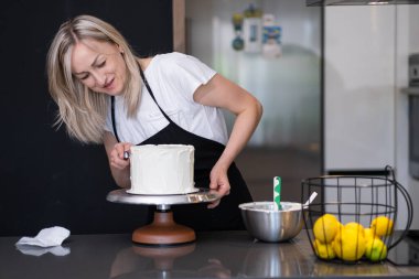 Mutlu kadın düğün kutlamaları için ev yapımı pasta yapmaktan zevk alıyor. Mutfak masasında beyaz mastikle pastayı kaplayan profesyonel pastacı.
