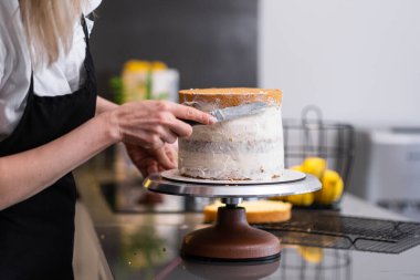 Deneyimli, kendi kendini pişirmiş pasta katmanlarının etrafına lezzetli krem sürerek siyah önlüklü bir kadın bıçakladı. Şekerlemeler üzerine lezzetli hamur işleri yapma sürecini detaylı bir şekilde gösteriyor.