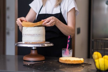 Mutfakta duran laktozsuz ürünlerden ev yapımı hamur işi yapan kremalı kadın kremalı pasta tabakalarını birbirine bağlayan siyah önlüklü profesyonel bir şekerci.