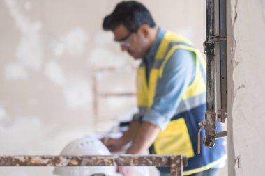 Odaklanmış profesyonel üniforma uzmanı apartmandaki oda yenileme işlemi sırasında inşaat güvenlik ekipmanlarının yanında duran belgelerle çalışıyor.