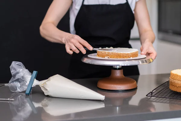 Stock image Woman in black apron smearing organic sugar free cake layers with delicious cream using kitchen utensil confectioner standing at table making custom pastry for wedding celebration