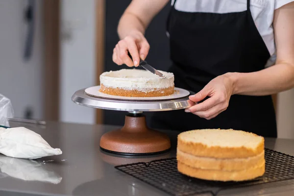 stock image Skilled female confectioner smearing organic cake layers with knife standing at table in modern kitchen at home housewife enjoying cooking delicious confectionery for customers