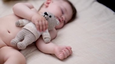 Sevimli tombul bebek, elinde örgü ayı oyuncağıyla uyuyordu. Gözleri kapalı tatlı çocuk, çocuk odasında rahat bir yatakta kestiriyordu.