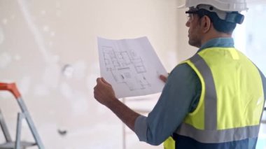 Çelik yelek giymiş, çizim projesine odaklanmış işçiler eski püskü duvar ve merdiven inşaatı güvenlik ekipmanları ve evdeki yenileme işlemleri ile aynı odada duruyor.