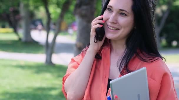 Wanita Ceria Dengan Rambut Longgar Gelap Berbicara Ponsel Memegang Tablet — Stok Video
