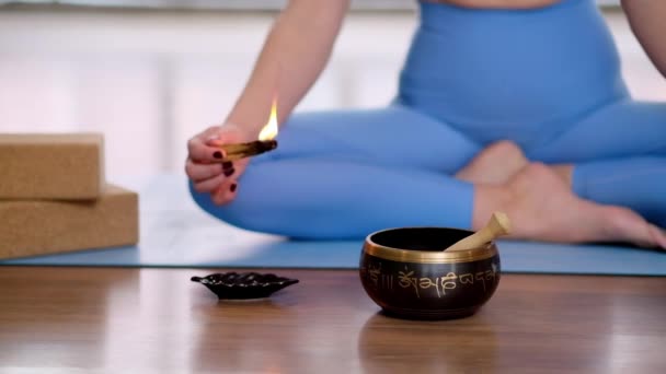 荷花女子坐在蓝色垫子上静坐静坐燃烧着香气棒和藏语唱盘 上面有提比坦语的符号 珠宝荷花 旁边是轻盈的瑜伽工作室 — 图库视频影像