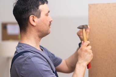 Mobilya imalatı ve nakliye firması işçisi. Tulum giyer, çivi çakar. Yatak odası için ahşap gardırop yapar.