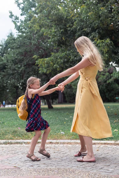 Joyful mother and daughter dance carefree in park young woman and girl hold hands spinning and laughing happily parent and kid have fun together outdoors side view