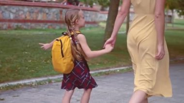 Küçük mutlu liseli kız, anne elini tutuyor. Şehir parkında aynı okula gidiyor. Kızı okula götürüyor.