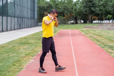 Eşofmanlı bir adam telsiz kulaklık takıyor şehir spor salonunda yürüyor sarı tişörtlü düşünceli bir sporcu açık havada müzik eşliğinde antrenman yapıyor.