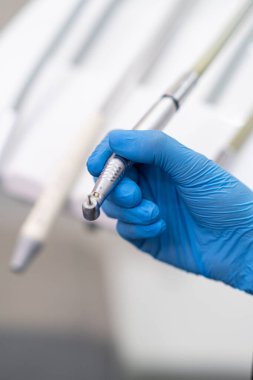 Diş hekiminin elindeki matkapla stomatoloji kliniğindeki dişçi muayenehanesindeki çağdaş diş makinesi panelinin üzerinde modern aletler kullanarak hasta diş işleme işlemi yapıyor.