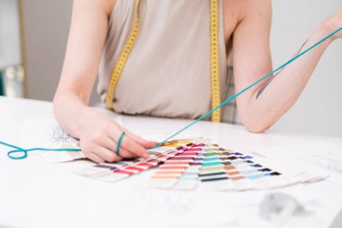 Mezuralı tasarımcı, elbise dikme atölyesindeki kumaş rengi ile atölyedeki kumaş rengi karşılaştırıyor. Stüdyoda zarif kıyafetler için kumaş gölgesi dikiyor.