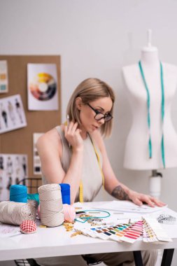 Moda stüdyosunun terzisinin tasarımcı işyerindeki makrame iplik bobinleri ve renk örnekleri terzi atölyesindeki kadın işyeri atölyesinde elbise eskiziyle çalışıyor.