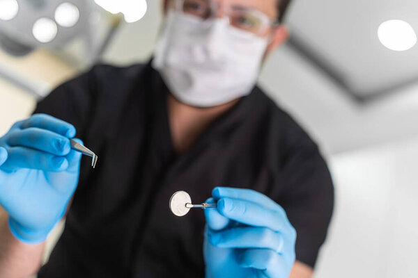 Skilled male dentist in black uniform examining patient oral cavity using metal tongs and round mirror at appointment in stomatology center teeth care procedure
