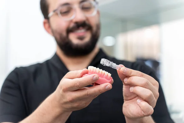 Neşeli dişçi yapay insan çenesi üzerinde net hizalamalar gösteriyor stomatoloji kliniği uzmanında yenilikçi diş düzeltmesi sunuyor tıbbi cihazları kapalı tutuyor