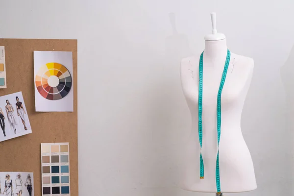 Mezura ve tahta ile manken, atölyedeki terzi teçhizatında dikim stüdyosu moda tasarımcılığında beyaz duvar tarafından çizilmiş eskizler.