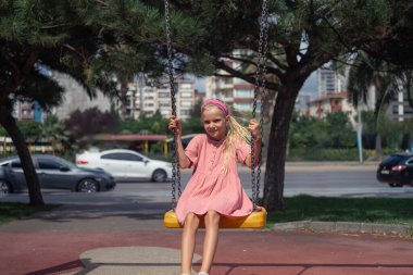 Canlı bir çocuk, pembe giyinmiş, çocuk parkındaki salıncakta saf neşe buluyor.. 