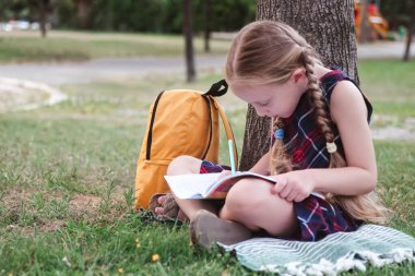 Doğa sınıfı: mutlu bir liseli kız, sıcak bir sonbahar günü yeşil bir şehir parkında bir ağacın altında ders çalışıyor.. 