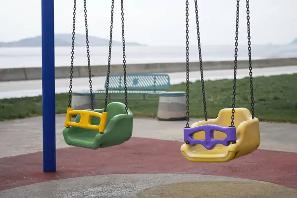 Multicolored plastic swings on metal chains in children playground on waterfront near sea on summer day equipment for kids entertainment and leisure activity