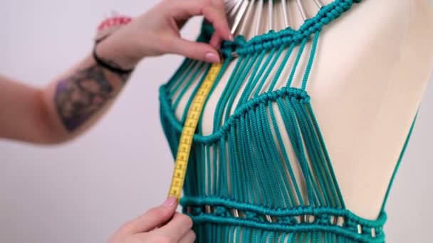デザイナーは ドレスメイキングワークショップで糸で作られた未完成の衣服にブロンドの女性を縫うダミーにユニークな緑のマクラメのドレスを作成します — ストック動画