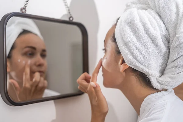 Home beauty ritual: A womans reflection in the mirror as she diligently applies moisturizer, elevating her daily skincare.