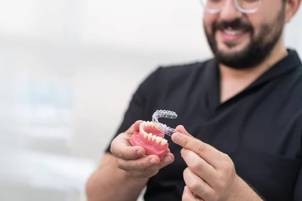 Neşeli ortodontist, modern stomatoloji kliniği sakallı dişçisinde dişleri düzeltmek için suni alt çeneye şeffaf hizalayıcılar koyuyor.