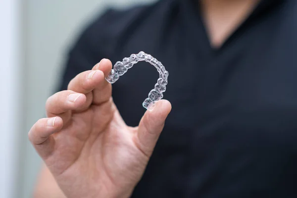 Dentist in black uniform holding clear aligners of orthodontic treatment tool for teeth maintaining in stomatology center doctor holding modern braces closeup