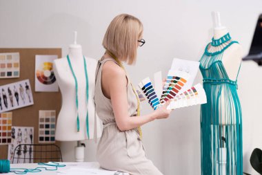 Renkli kumaş ve kıyafet eskiziyle kadın moda tasarımcısı atölye atölyesinde atölye atölyesinde atölye yaratıcı terzisinde manken elbisesi üzerinde çalışıyor.